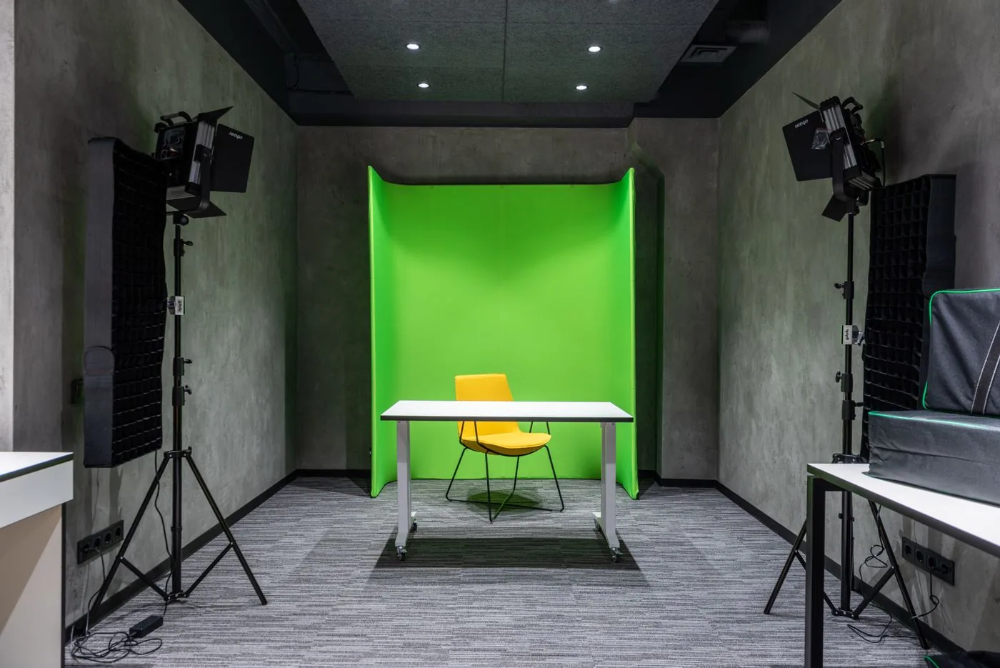 A green screen studio with lighting stands, a yellow chair and a white table