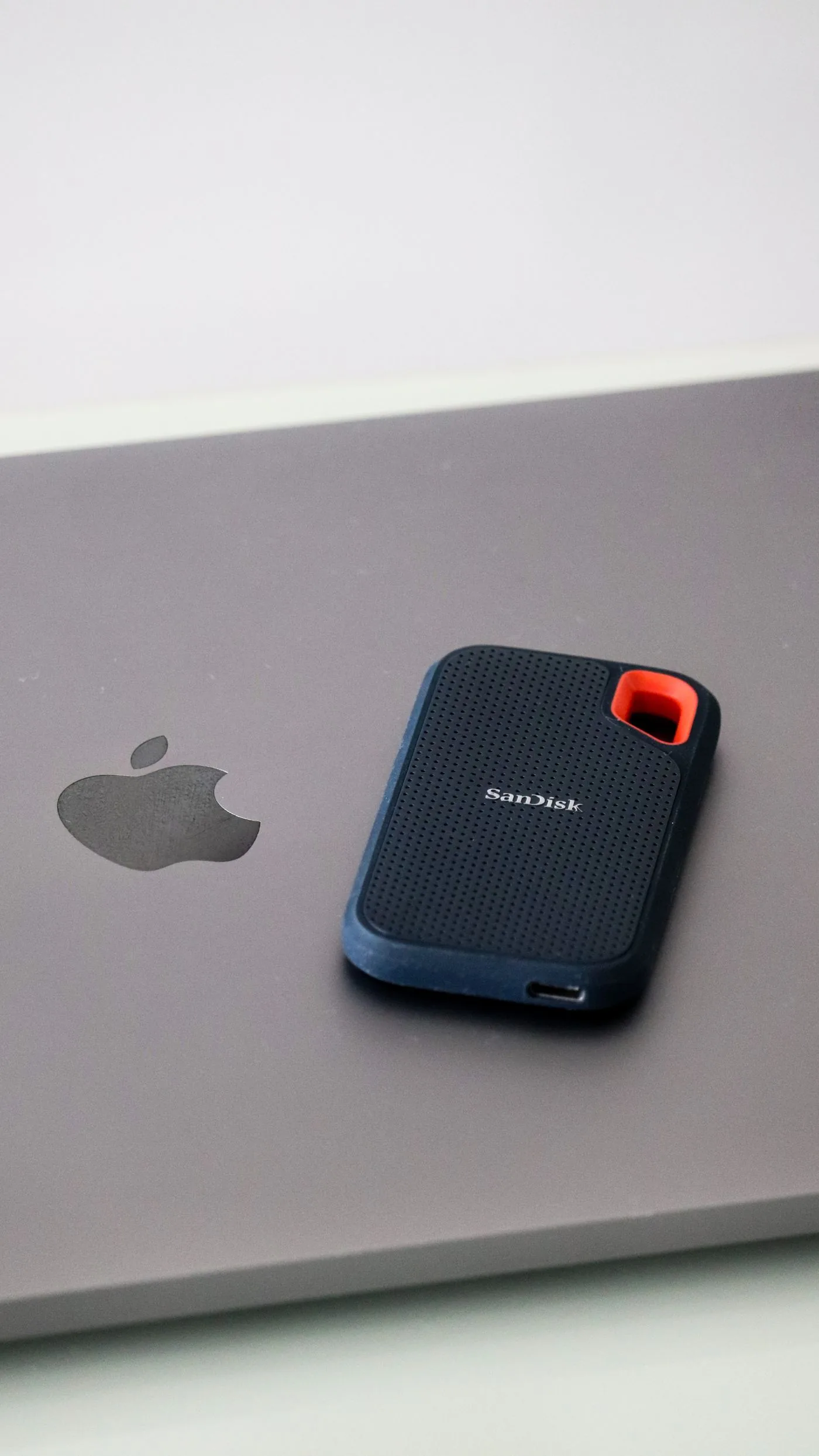 A portable SanDisk SSD resting on a laptop keyboard beside its cable